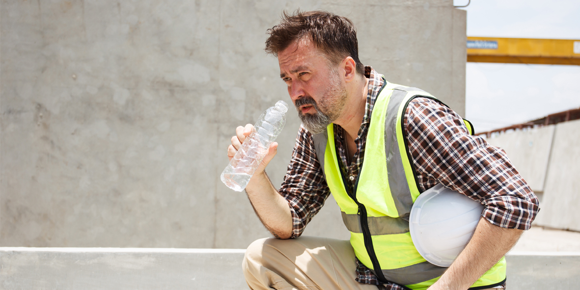 Dangerous from heat wave during working outside the building. Caucasian male construction worker resting and drinking water from bottle in a very hot day. Heat stroke health problem.
