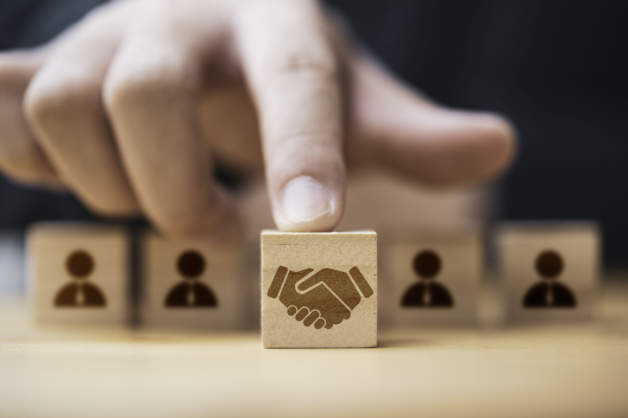 Hand putting hand shaking which print screen on wooden cube block in front of human icon for business deal and agreement concept.